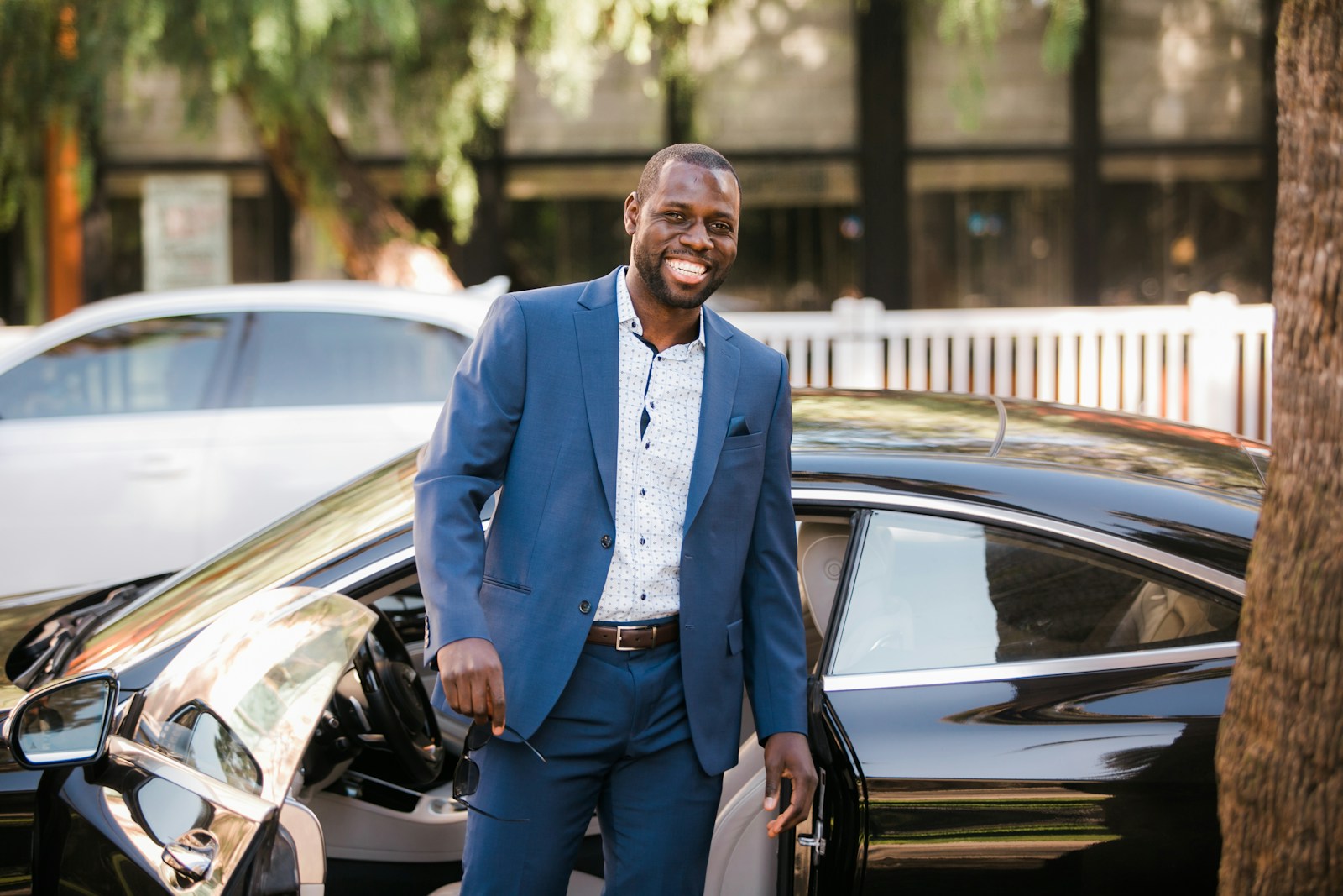 man in blue suit standing beside black car knowing his property worth